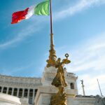 The iconic Altare della Patria with Italian flag waving under clear blue sky in Rome, Italy.