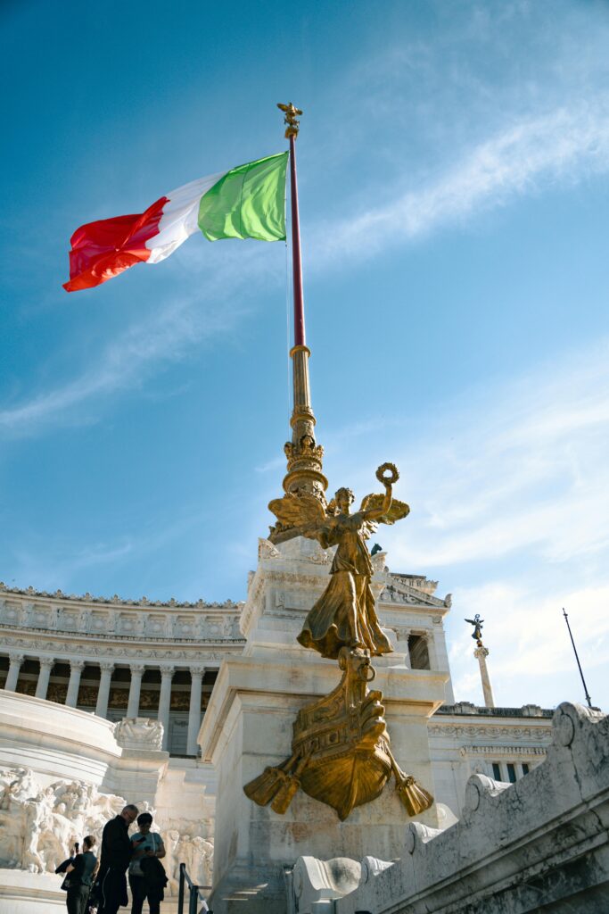 The iconic Altare della Patria with Italian flag waving under clear blue sky in Rome, Italy.